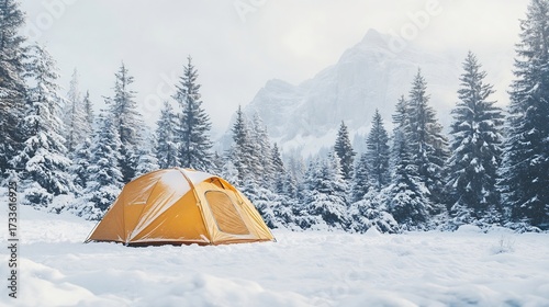 Rugged four season tent covered in light snow on a high altitude campsite surrounded by pine trees and mountain peaks made for winter camping in extreme conditions