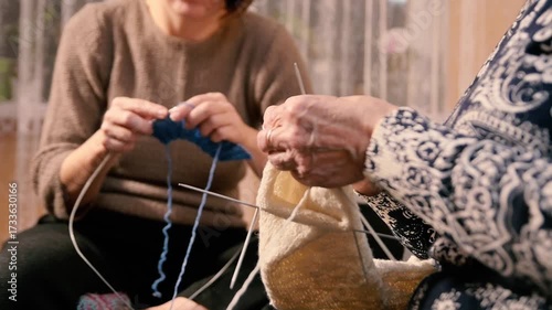 Close-up of two women's hands engaged in knitting, crafting cozy garments with yarn and needles. A timeless hobby showcasing handmade artistry and shared creative passion.