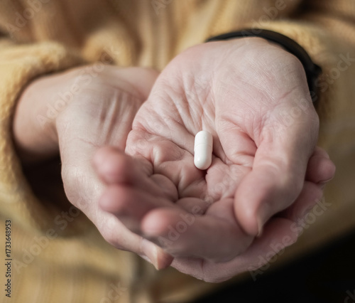 An elderly lady holds one capsule of medicine in her hands