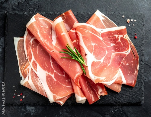 Slices of cured ham on a dark stone platter