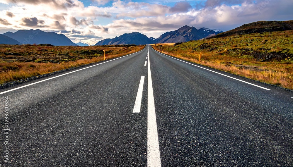 Naklejka premium Asphalt Road Leading to Mountain Range Under Cloudy Sky in Iceland Landscape