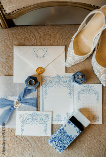 Elegant vintage style wedding details. Wedding invitation, pair of wedding rings, women's shoes and perfume on vintage fabric, showcasing romantic blue and white wedding stationery and accessories