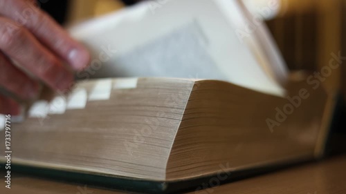 hand flipping pages of thick dictionary book on library desk. Concept of education, research, knowledge, study, learning resource, language reference, academic information access.