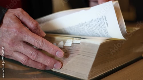 hand flipping pages of thick dictionary book on library desk. Concept of education, research, knowledge, study, learning resource, language reference, academic information access.