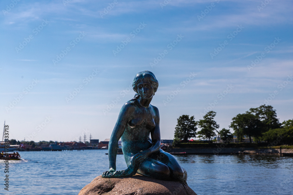 Fototapeta premium Copenhagen, Denmark 07-20-2025 The bronze statue of the Little Mermaid sitting on a rock by the waterside at the Langelinie promenade in Copenhagen. The small and unimposing statue is an icon in town.