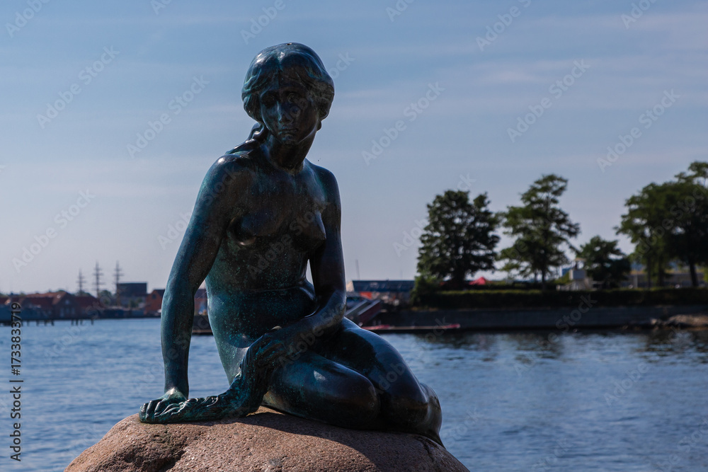 Obraz premium Copenhagen, Denmark 07-20-2025 The bronze statue of the Little Mermaid sitting on a rock by the waterside at the Langelinie promenade in Copenhagen. The small and unimposing statue is an icon in town.