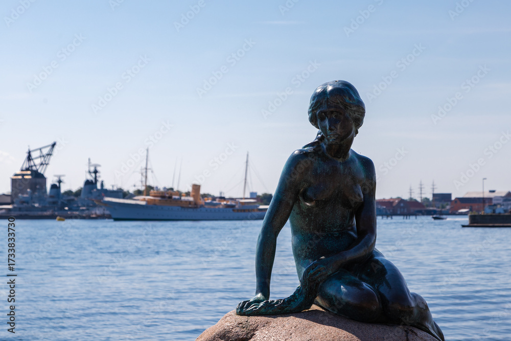 Obraz premium Copenhagen, Denmark 07-20-2025 The bronze statue of the Little Mermaid sitting on a rock by the waterside at the Langelinie promenade in Copenhagen. The small and unimposing statue is an icon in town.