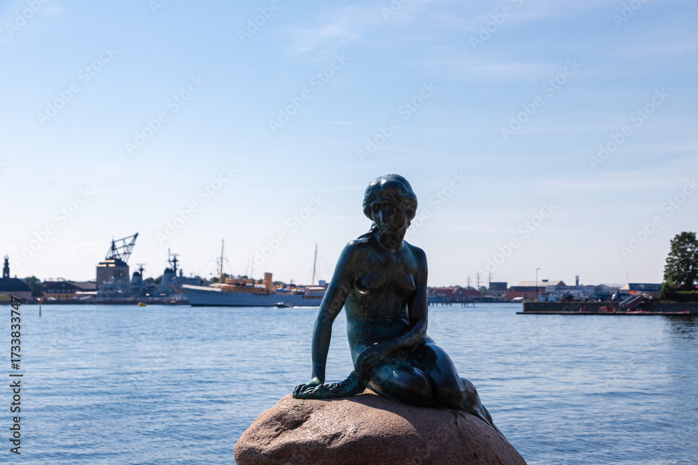 Obraz premium Copenhagen, Denmark 07-20-2025 The bronze statue of the Little Mermaid sitting on a rock by the waterside at the Langelinie promenade in Copenhagen. The small and unimposing statue is an icon in town.