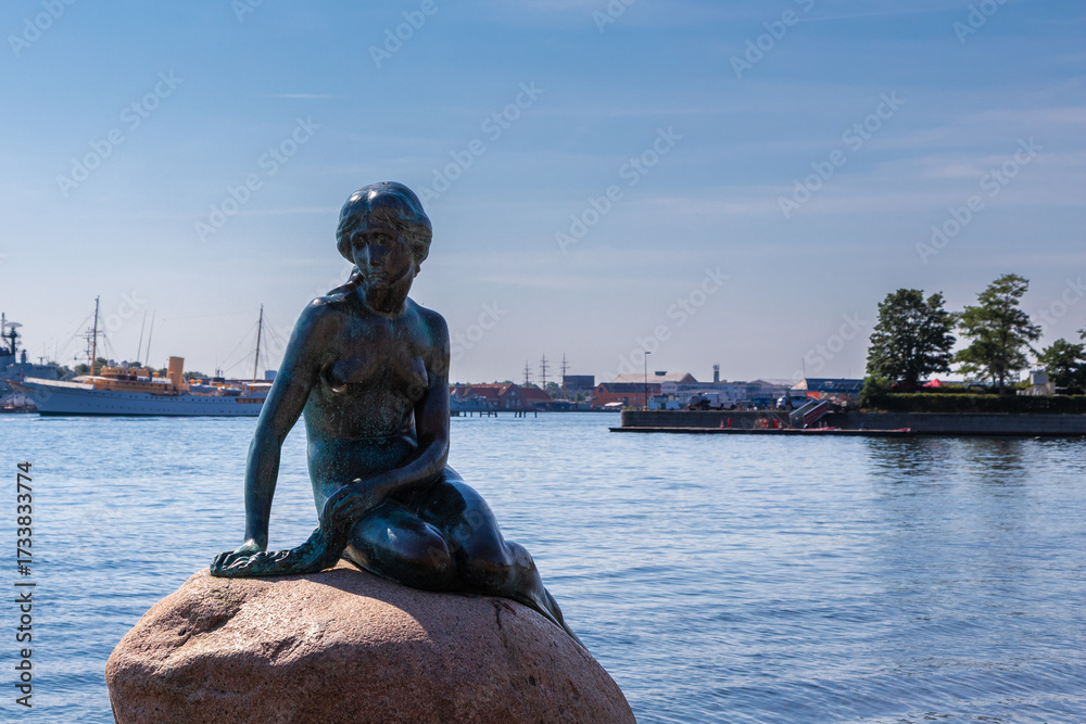 Obraz premium Copenhagen, Denmark 07-20-2025 The bronze statue of the Little Mermaid sitting on a rock by the waterside at the Langelinie promenade in Copenhagen. The small and unimposing statue is an icon in town.