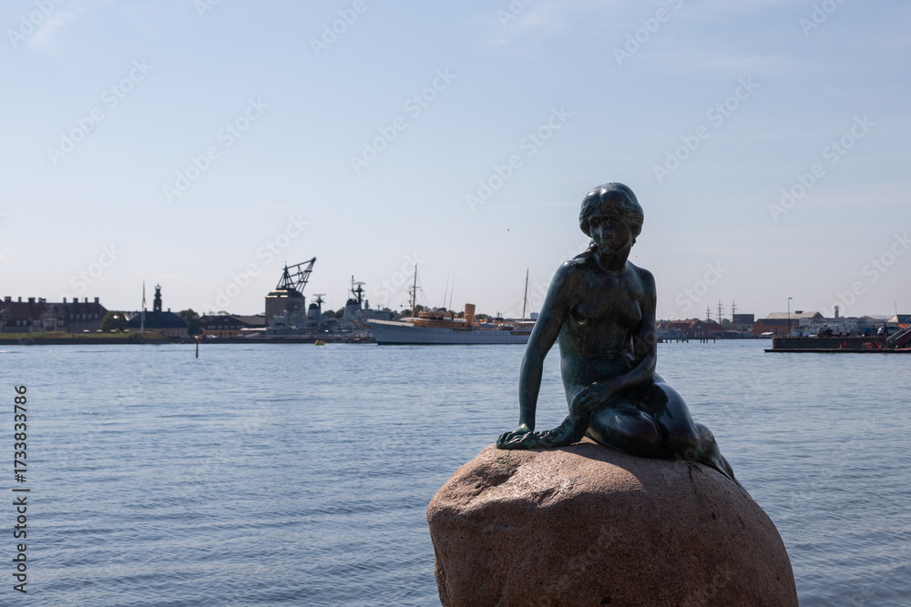 Obraz premium Copenhagen, Denmark 07-20-2025 The bronze statue of the Little Mermaid sitting on a rock by the waterside at the Langelinie promenade in Copenhagen. The small and unimposing statue is an icon in town.