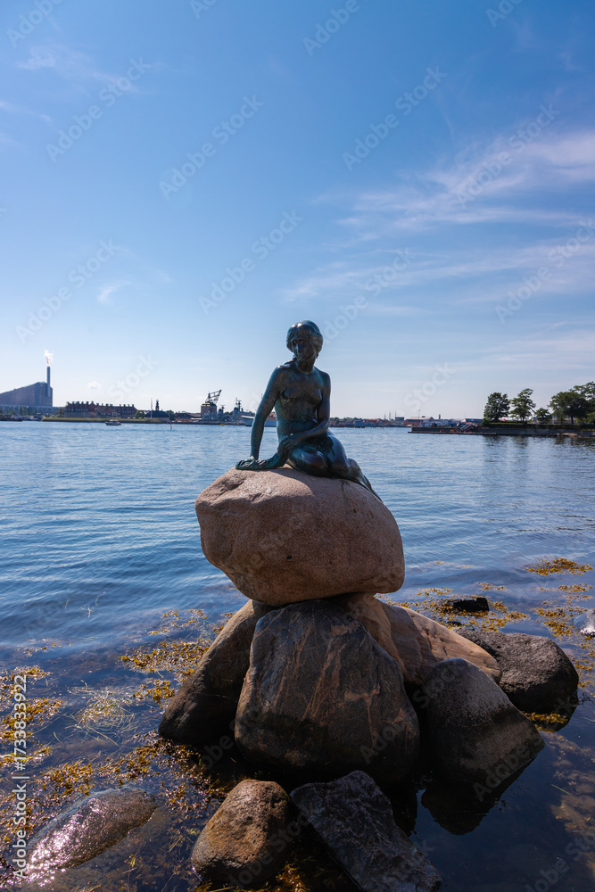 Obraz premium Copenhagen, Denmark 07-20-2025 The bronze statue of the Little Mermaid sitting on a rock by the waterside at the Langelinie promenade in Copenhagen. The small and unimposing statue is an icon in town.