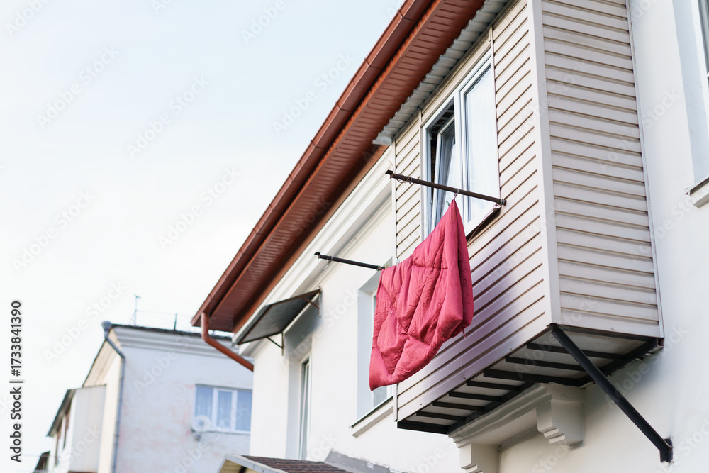 Naklejka premium Bright red blanket hanging outside a white house on a sunny day in an urban neighborhood