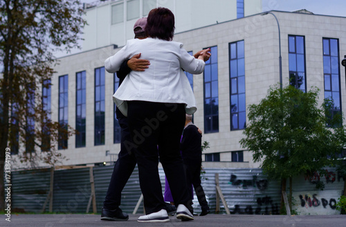 Couple dances joyfully in a city square during an evening gathering amidst modern buildings and greenery