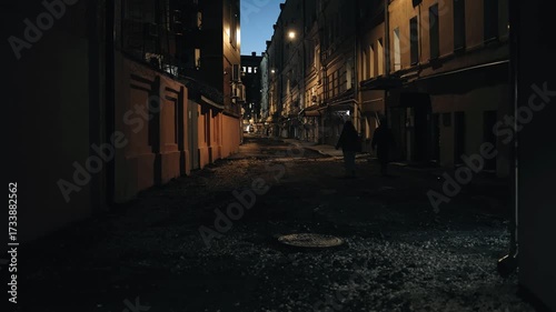 A few people are walking down a dark, scary alley, moving away from the camera.