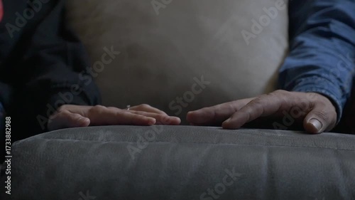 Close-up of the hands of a couple (a man and a woman) resting silently on a sofa.