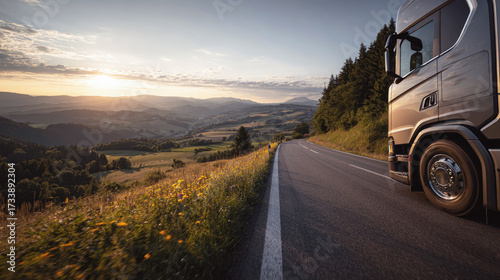 Truck driving on scenic mountain road at sunset, overlooking valleys, fields and forests, symbolizing transportation, logistics and travel through nature.
