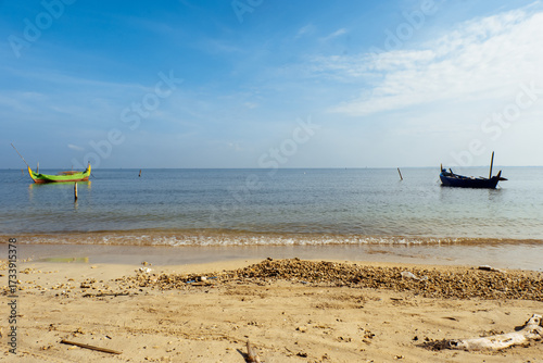 Fishing boats rest under a bright blue sky on a peaceful tropical beach.