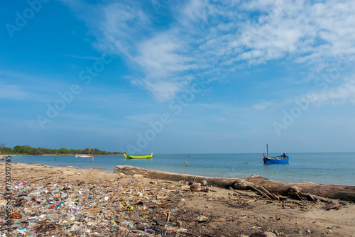 fishing boats docked on a tropical beach with trash along the shore, fisherman village