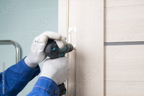 the master installs an interior door by screwing the hinge to the doorway, close-up, master's hands in gloves