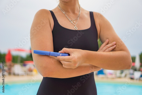 Bild auf Leinwand close up of a woman in a black swimsuit holding a blue injector pen Ozempic for