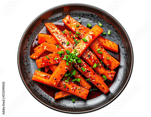 Top-down view of glazed carrot sticks on a dark plate, garnished with herbs