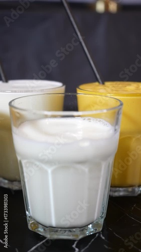 Fresh milk pouring into a glass surrounded by other colorful milkshakes drinks