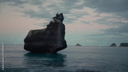 a lone rock in the sea at sunset.