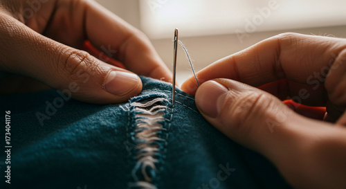 Close-up of hands repairing torn denim with needle and thread, representing sewing, mending clothes, craftsmanship, and sustainable fashion practices.