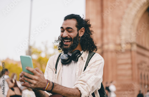 Man laughs loudly while looking at phone, showing surprise, delight and digital happiness in tech-enabled urban lifestyle.