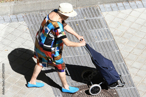 Fotografie Mujer empujando carrito de compra, ropa colorida, zapatos azules y sombrero de p