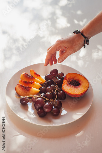 Female Hand Reaching for Peach and Grapes on White Plate, Sardinia