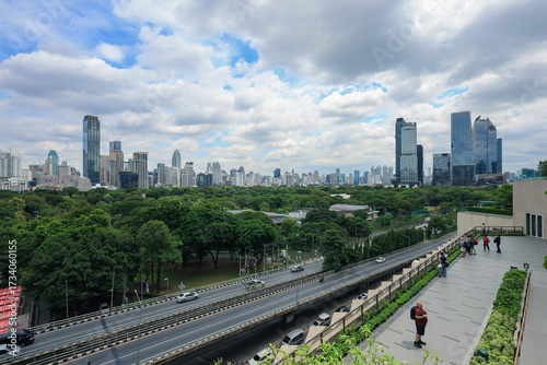 Wide-angle view of traffic on city street and green spaces of a park with the many skyscrapers in the background of the central business district of Thailand.