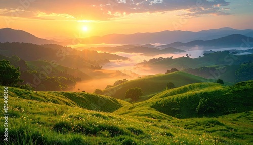 Aerial View of Rolling Green Hills Illuminated by Golden Sunrise Light Bathed in Warm Hues and Mist Covered Mountains in a Serene Landscape