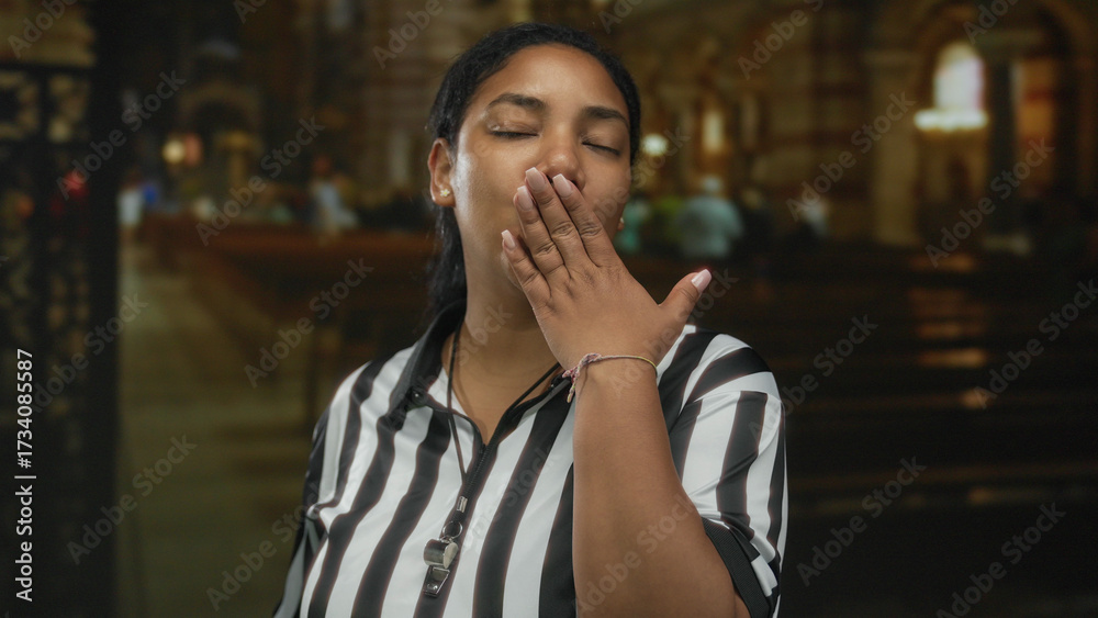 Fototapeta premium Woman referee in striped jersey blows kiss indoors at ornate church interior with visible whistle; love.