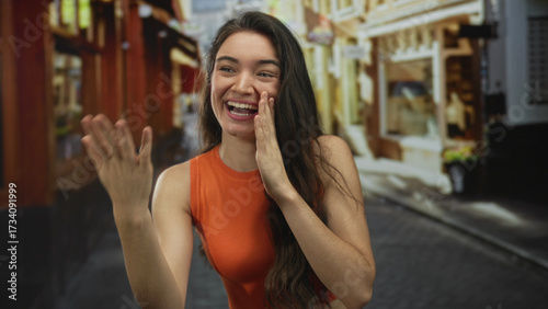 Young hispanic woman calls out with hand to mouth on a sunny cobblestone street; communication urgency. Free Download Young hispanic woman calls out with hand to mouth on a sunny cobblestone street; communication urgency. - GFXLoad