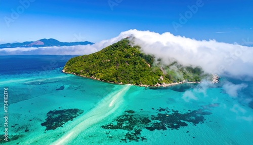An aerial view captures a tropical island, partially shrouded in mist, nestled in vibrant turquoise waters.  A sandbar extends from the island's shore