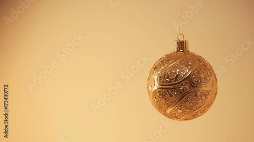 Elegant golden Christmas ornament with intricate decorative patterns hanging on a string against a warm gradient background.