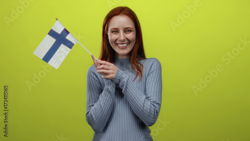 Woman holding finnish flag cheerfully against vibrant yellow background, embodying national pride and joyful expression.