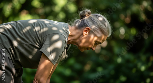 Profile of a healthy mature woman with gray hair in a bun, focused as she bends over during an outdoor activity in a sunlit garden