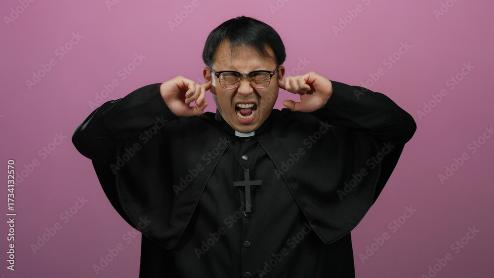 Obraz premium Man in black robe covering ears with hands standing against pink wall expressive gesture emotion glasses religious cross isolated background