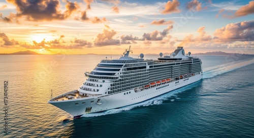 Luxury cruise ship sails through turquoise waters at golden hour sunset. The white vessel creates wake trails as it navigates tropical seas with distant mountains on the horizon.