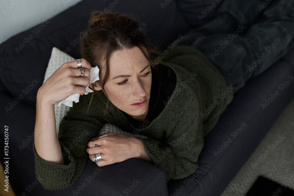 Obraz premium Young woman struggles with feelings of sadness while lying on her couch at home