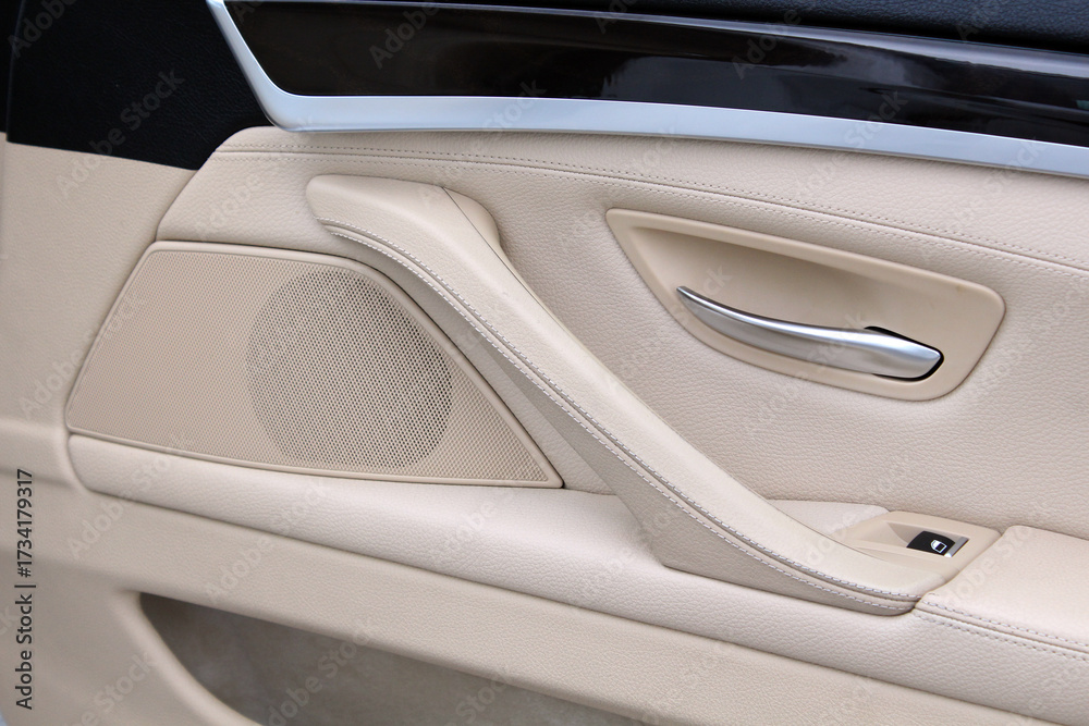 Φωτογραφία Close-up of beige luxury car door interior featuring stitched leather trim, silver door handle, integrated speaker and premium soft touch materials