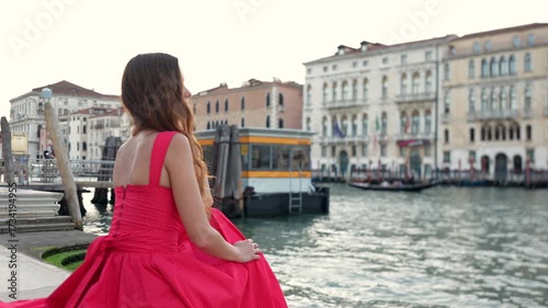Tourist in red summer dress by canal looking at historic palaces