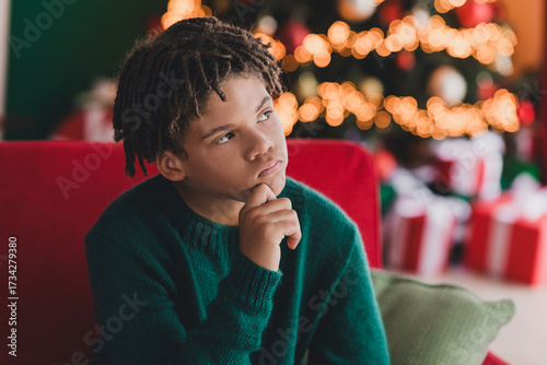 Fotografi Thoughtful boy in cozy home during Christmas season amid festive tree lights and