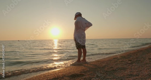 A child on the seashore at sunset enjoys the gentle waves. A beautiful golden sunset illuminates the little boy standing at the water's edge, feeling the gentle waves wash over his feet.