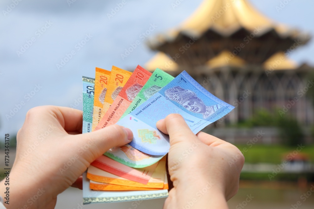 Fotografie Hand holding Malaysian ringgit paper money with Kuching city skyline in background