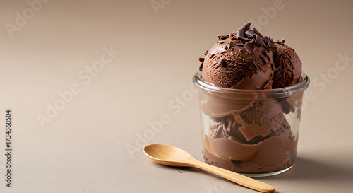 A creamy dark chocolate gelato served in a small glass jar with a wooden spoon on the side, topped with chocolate shavings.
