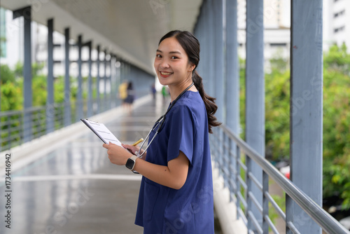 Asian woman nurse holding clipboard smiling in hospital corridor Free Download Asian woman nurse holding clipboard smiling in hospital corridor - GFXLoad