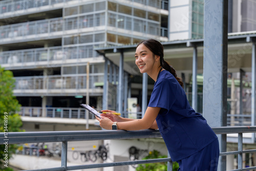 Asian nurse in scrubs holding clipboard smiling outdoors Free Download Asian nurse in scrubs holding clipboard smiling outdoors - GFXLoad